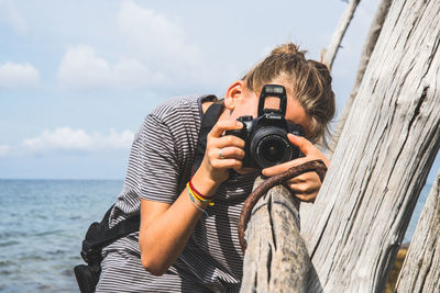 Young man photographing with camera against sky