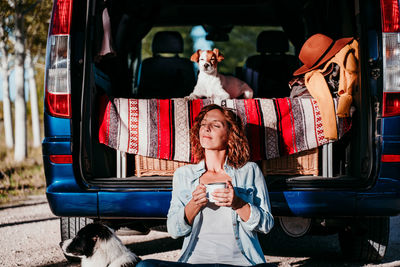 Woman with eyes closed holding mug while sitting by camper trailer