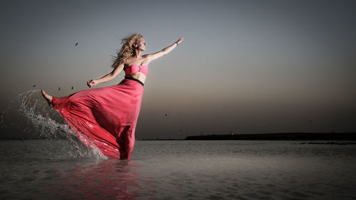 Full length of woman splashing water while standing in sea during dusk