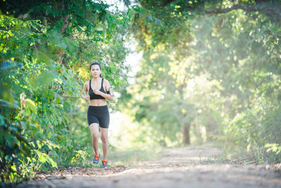 Full length portrait of young woman jogging on dirt road amidst trees