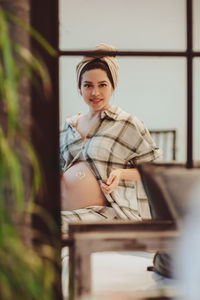 Portrait of pregnant woman seen through window