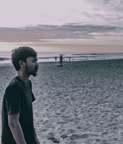 Side view of man standing on beach against sky during sunset