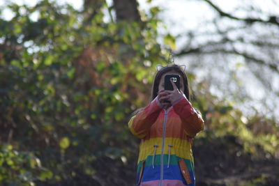 Low angle view of girl using mobile phone against tree