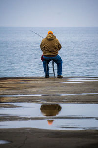 Full length rear view of man sitting on chair at pier