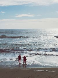 Rear view of couple walking on shore at beach against sky