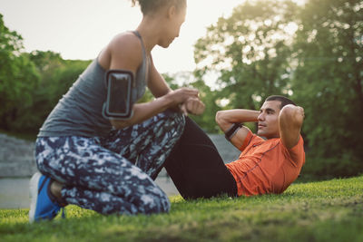 Woman kneeling and looking at man doing sit-ups at park