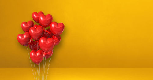 Close-up of red rose on table against yellow background