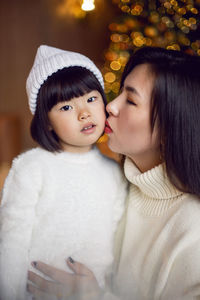 Beautiful korean mom and baby daughter sitting in white knitted sweaters at the christmas tree