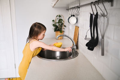 European child of 4 years with water for drink on bright kitchen in real interior, montessori