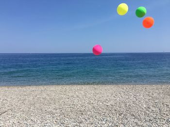 Multi colored balloons on beach against clear sky