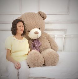 Woman with large teddy bear sitting on bed at home