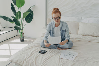 Young man using mobile phone while sitting on bed at home