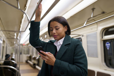 Young afro woman in metro train using mobile phone, biracial female suffer from smartphone addiction