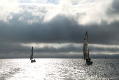 Sailboat sailing on sea against cloudy sky