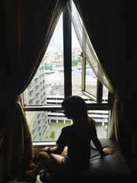 Rear view of woman looking through window at home