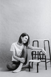 Portrait of young woman sitting on chair against wall