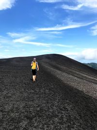 Rear view of mature woman with backpack standing on mountain against sky