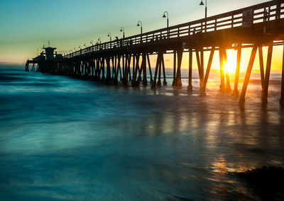 Silhouette pier over sea against sky at sunset