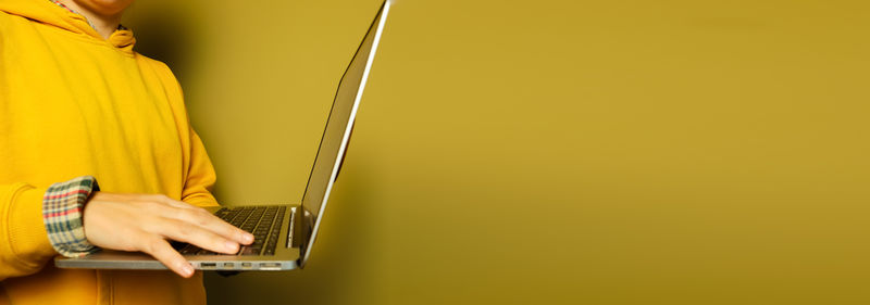 Midsection of woman using laptop against yellow background