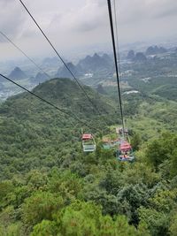 Overhead cable cars over trees against sky