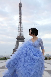 Woman standing on tower in city against cloudy sky