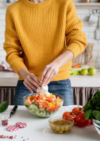 Healthy eating. front view of female hands making salad cutting feta cheese in the kitchen