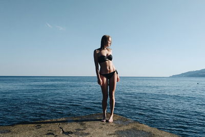 Full length of young woman standing in sea against clear sky