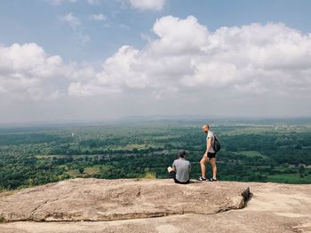 Full length of father and son sitting on mountain against sky