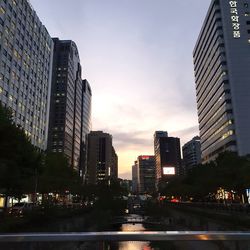 Illuminated buildings by street against sky at sunset