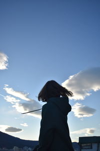 Low angle view of young woman standing against blue sky