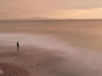 Man standing on beach against sky during sunset