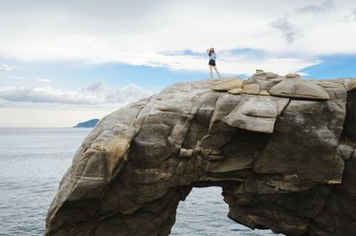 Woman standing on rock by sea against sky