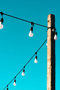 Low angle view of light bulbs hanging against clear blue sky