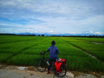 Rear view of man with bicycle standing at farm
