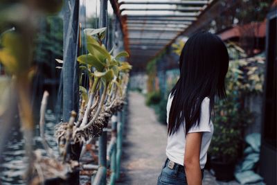 Side view of woman standing by plants in greenhouse
