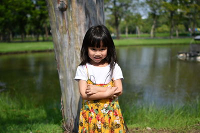 Portrait of smiling girl standing with arms crossed against lake