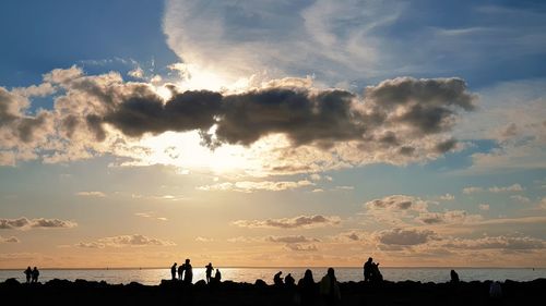 Silhouette people on beach against sky during sunset