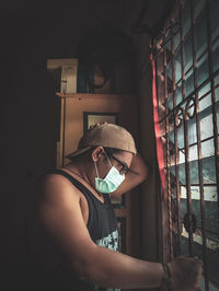 Side view of man wearing mask looking through window