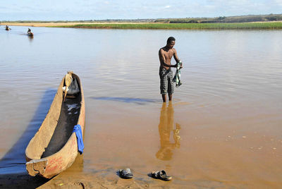 Rear view of shirtless man standing on lake