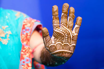 Midsection of bride with henna tattoo against blue background