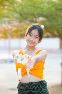 Portrait of smiling young woman drinking water while standing at park