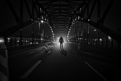 Rear view of person walking on illuminated bridge