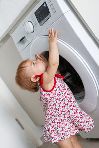 Side view of cute girl standing by washing machine