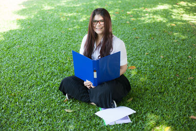 Portrait of young woman with file and papers sitting on grass