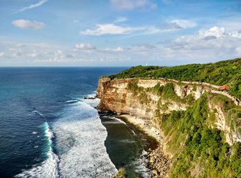 Waves rushing towards cliff against sky