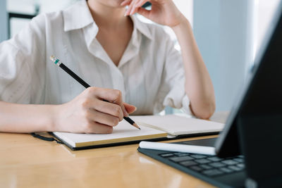 Midsection of woman writing in book at table