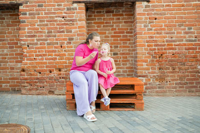 Rear view of woman sitting against brick wall