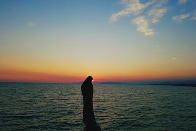 Silhouette man standing in sea against sky during sunset