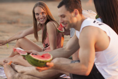 Happy couple with friends on the beach eating water melon