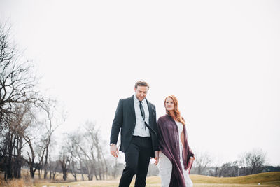 Couple walking on field against clear sky